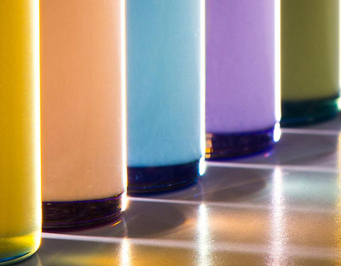 Photo of five glass tubes filled with colored fluids, from yellow, to orange, to blue, to violet, to green.