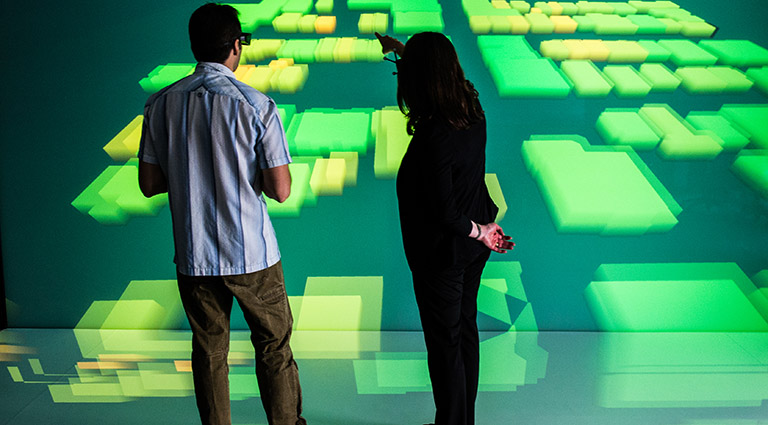 Photo of two researchers standing in front of a large-scale 3D visualization of a community energy grid model