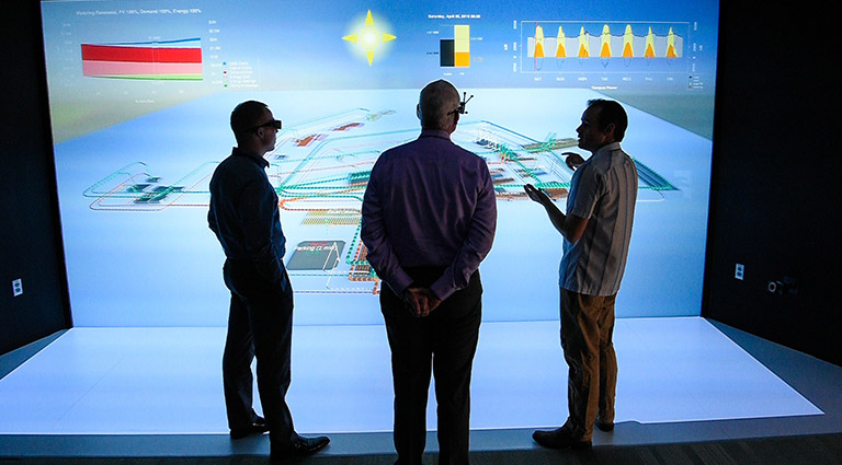 Photo of three researchers studying a large-scale 3D simulation of a campus-scale power system