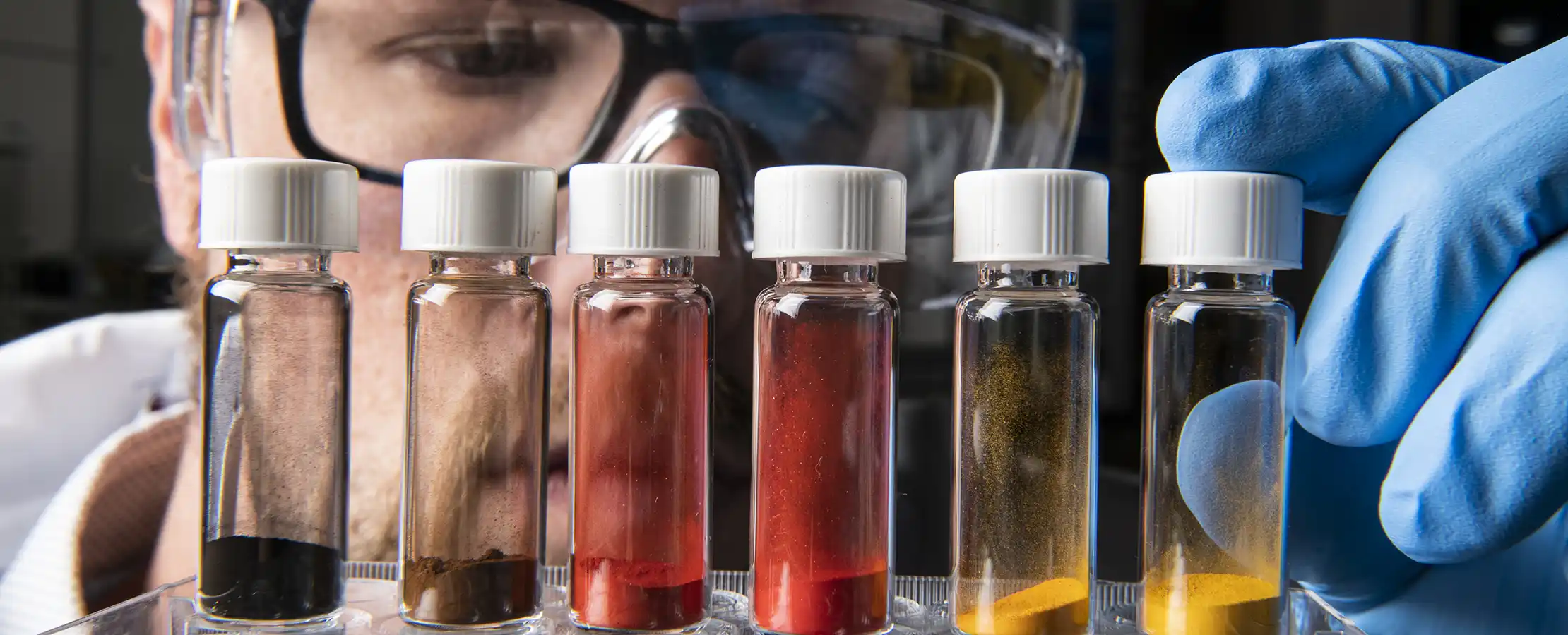 materials-science-hero-64686 A researcher examines six vials containing different powdered materials.