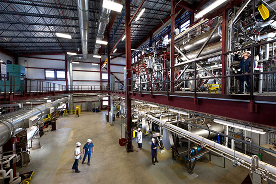 Photo of a large, warehouse-like, lab space with several people in hard hats operating equipment. 