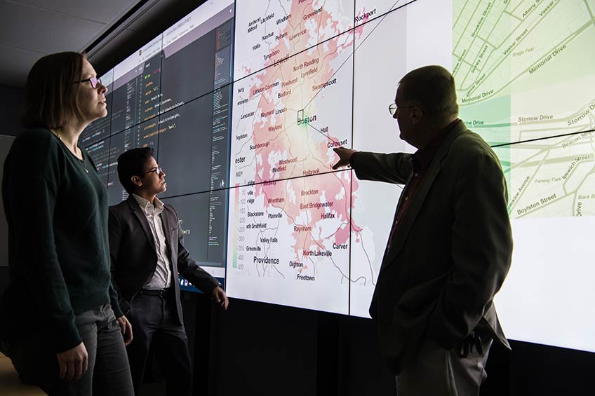 Three researchers view data on a large computer screen.