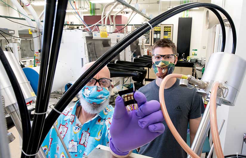 Two researchers hold up a dimethylammonium-containing wide-bandgap perovskite, flexible solar cell in a lab at NREL.