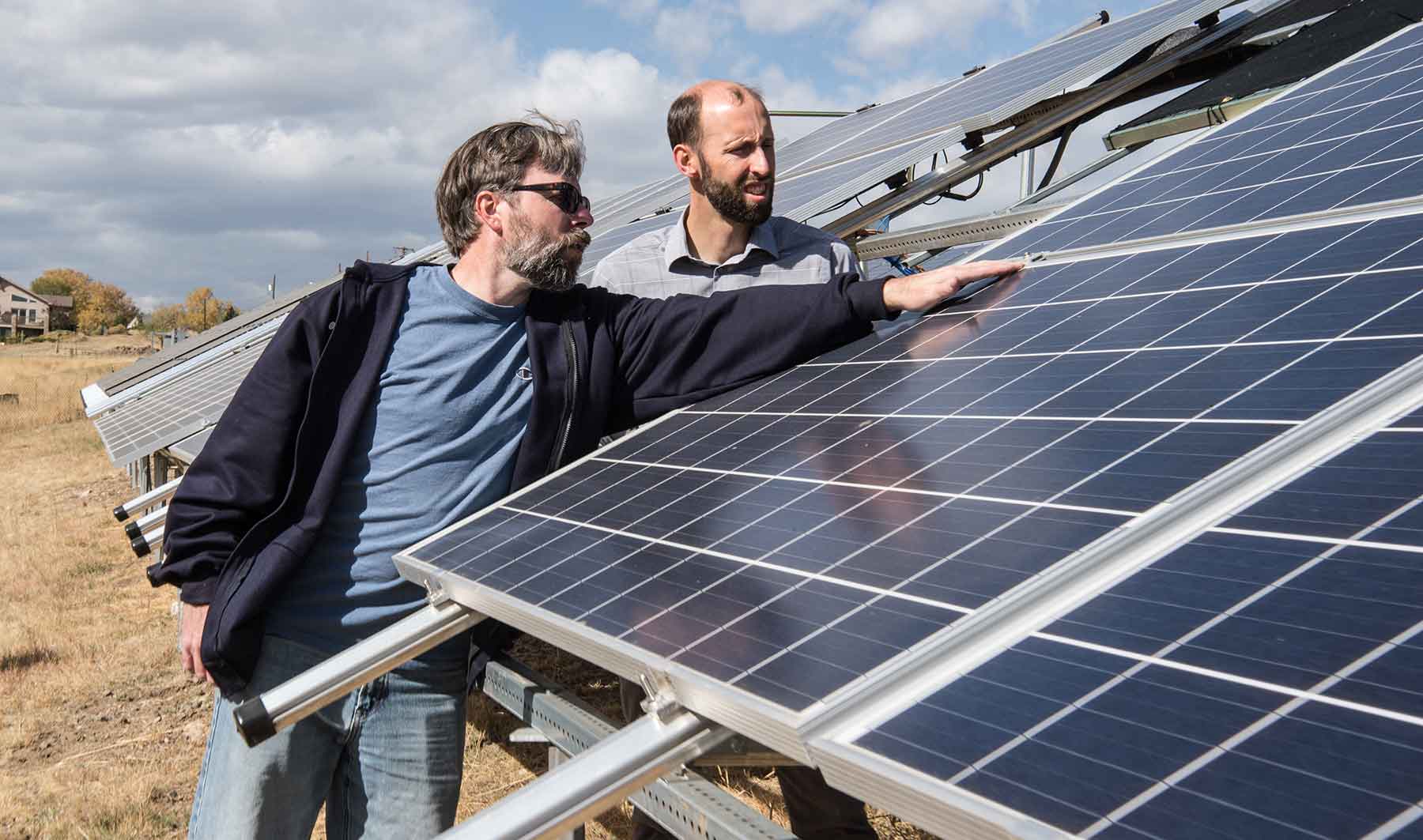 Two men examine solar modules set up in a field on the NREL campus.