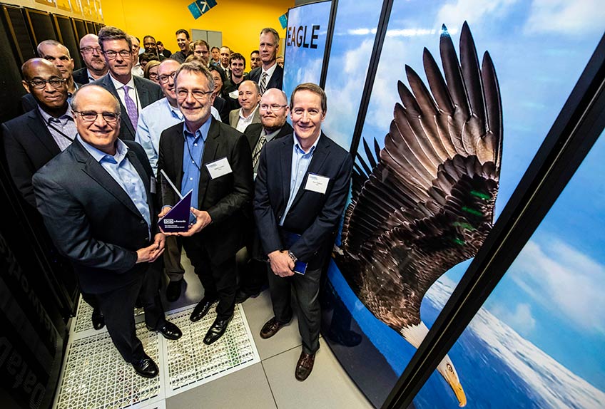Several researchers and organizational partners stand next to NREL's Eagle supercomputer.