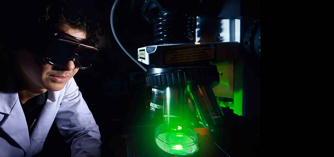 Photo of a scientist examining algae in a glass beaker.