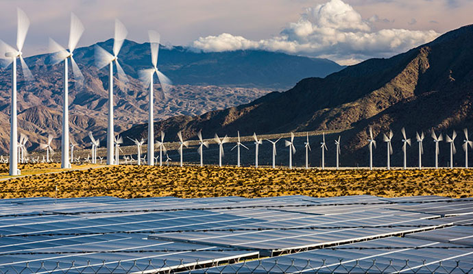 Solar panels in a field in the foreground with wind turbines in the background