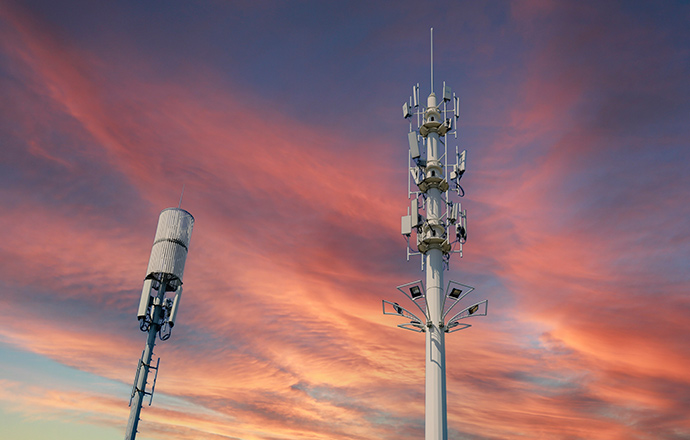 Photo of two 5G cell towers below orange clouds