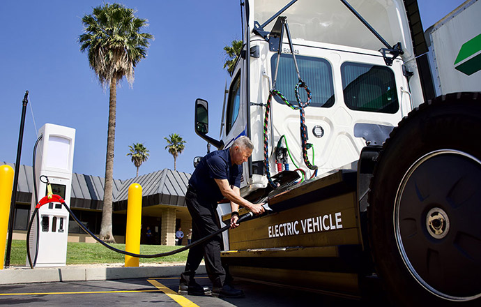 A man plugs a charging cable into a large electric truck.