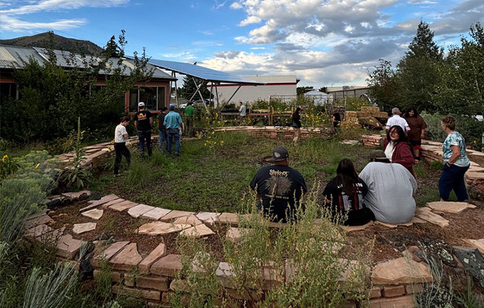 A group of people sit and walk through a garden encircled by stones.