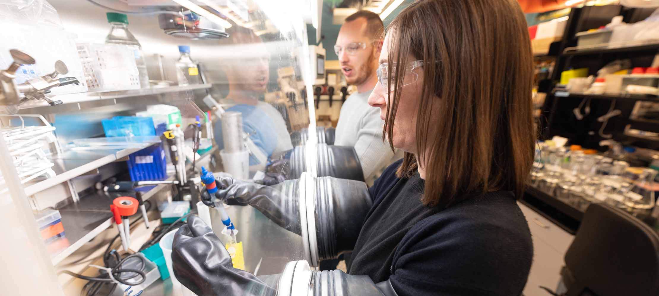 Two researchers in a lab work in a glovebox.