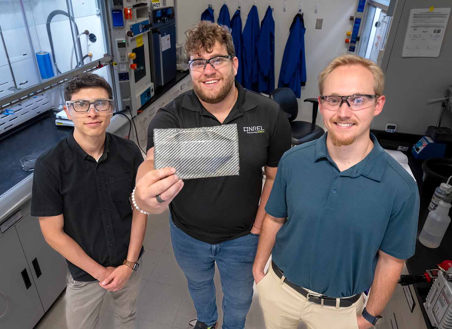 Three researchers in a lab hold up a recyclable carbon fiber composite sample.