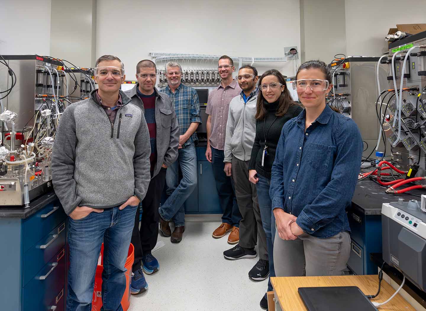 Seven researchers in safety goggles pose in a lab.