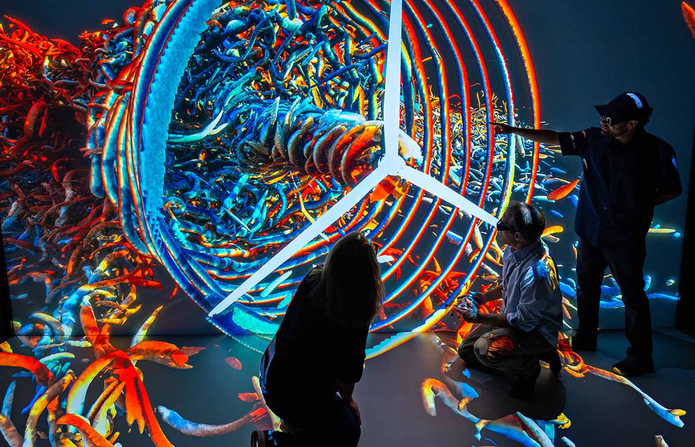 three researchers in silhouette interacting with a multicolor 3D visualization featuring a wind turbine.