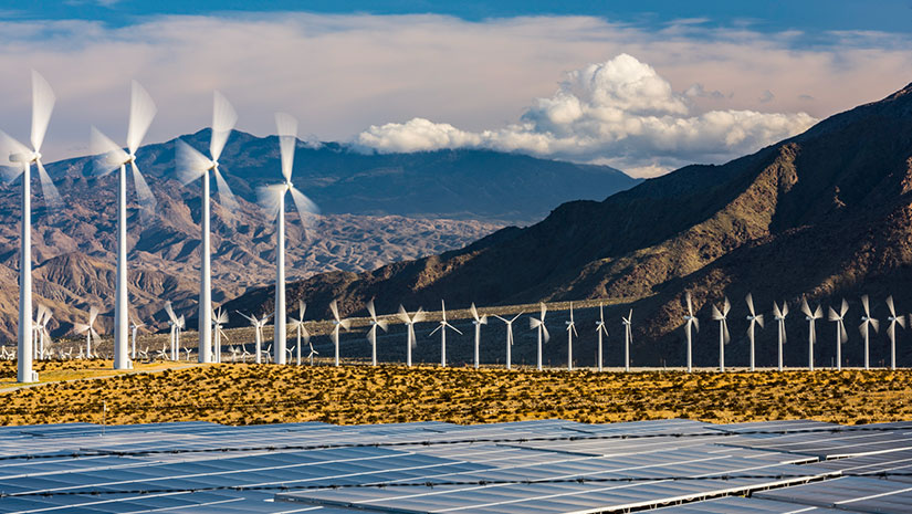 Wind turbines with mountains in the background and solar panel array in the foreground
