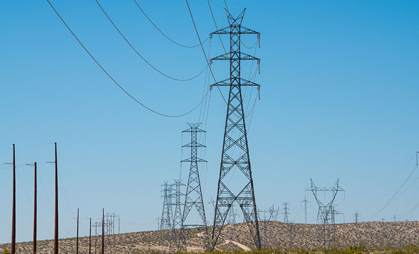 Photo of transmission lines in a desert that extend far into the distance.