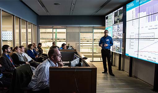 An NREL researcher presents on an electrolyzer grid integration demonstration in the control room of the Energy Systems Integration Facility.