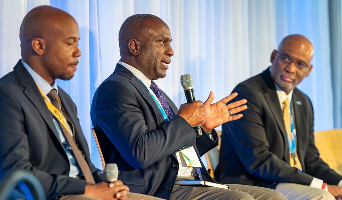 Three people sit on stage during panel discussion and speak into microphones.