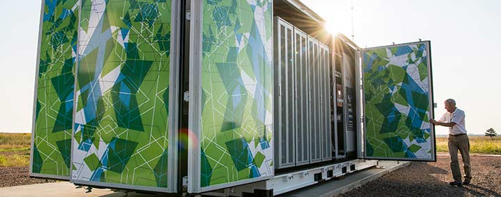 Photo of a man closing the door of a large, multicolored metal box that is roughly the size of a semi-truck trailer. Inside the box are batteries that make up a 1-megawatt battery energy storage system.