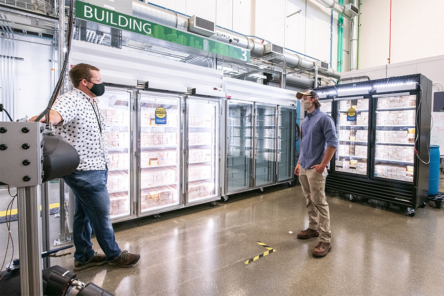 Two people work inside lab standing next to commercial refrigerators.