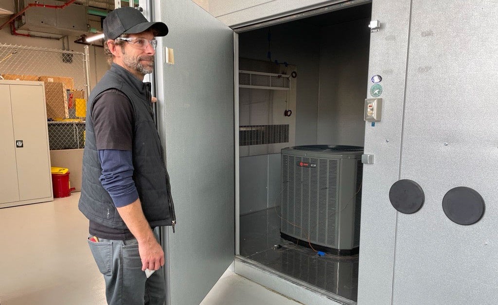 Photo of a person standing in front of an air conditioning unit inside a facility