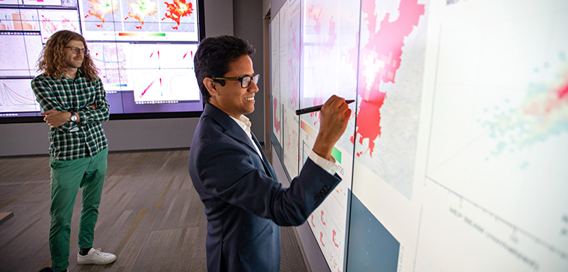 Photo of two researchers looking at large computer display and writing on it