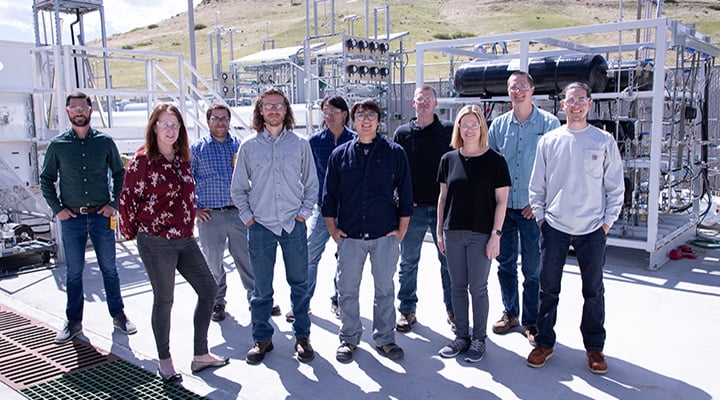 Group of researchers stand outside power grid system.