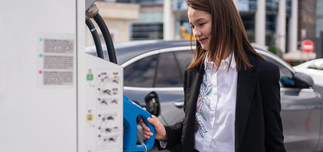 Young woman charging an electric car at public charging station.