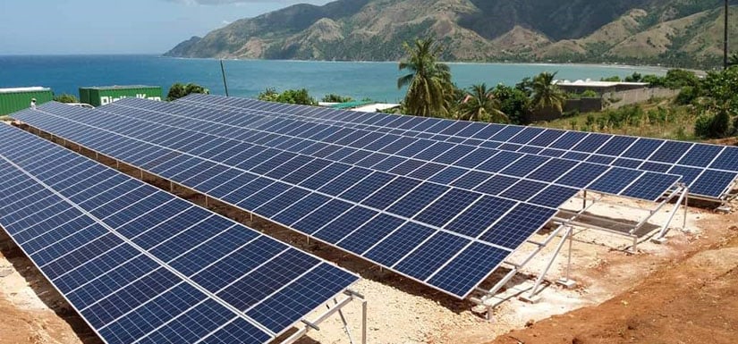 Solar panel arrays on shoreline with ocean in the background.