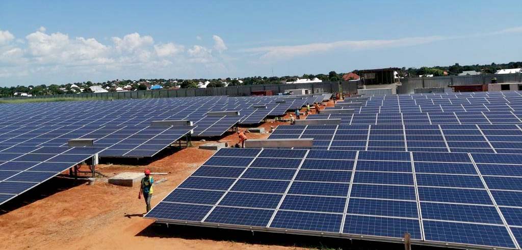 Person walks alongside solar panels on the ground.