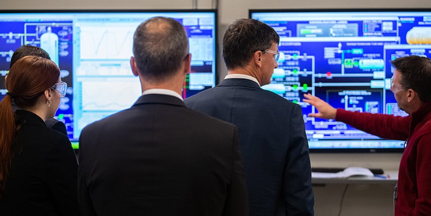 Photo of four people listening to a man explaining data on a computer screen.