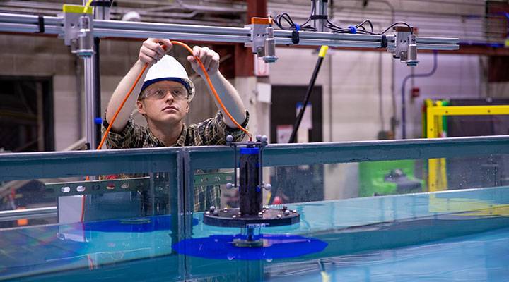 A person holds up a wire above the wave tank.