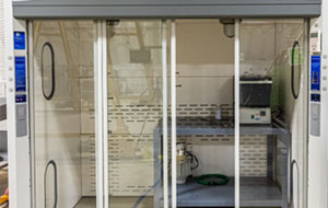 360tour-02-5648 Shelves are visible through the glass wall of a small, rectangular room accessible by a sliding glass panel door.