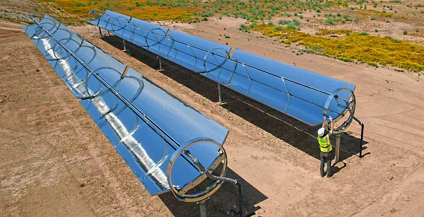 A man in a safety gear works on a reflective parabolic trough.