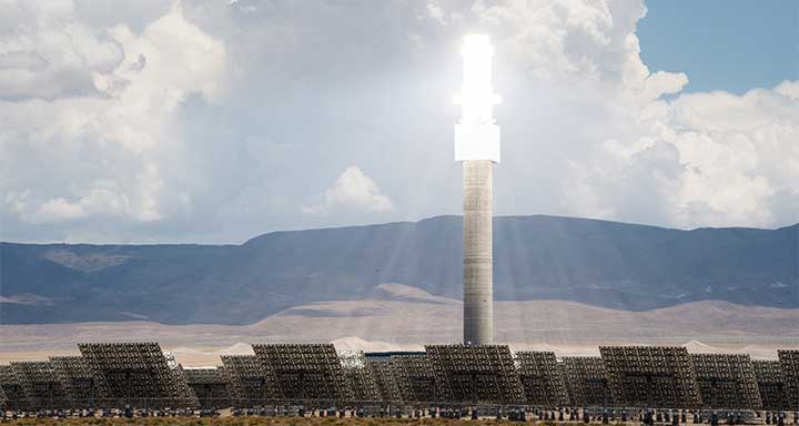 A heliostat glows in front of distant mountains.