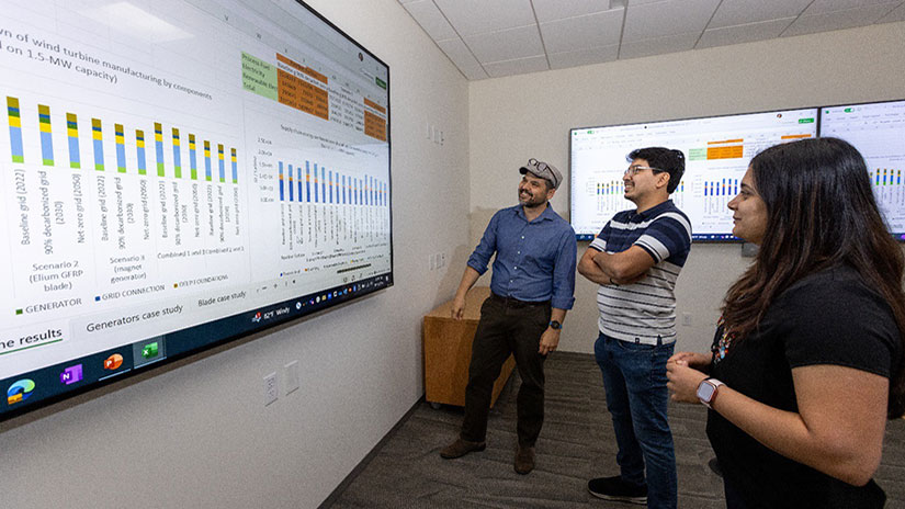 Three people stand and look at data on large display