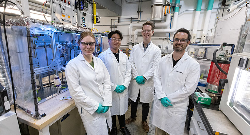 Four people in lab coats stand in front of equipment in a lab.