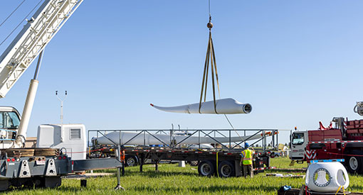 Wind turbine blade held up by crane in a field