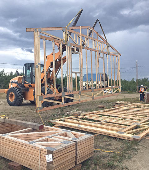 A crane lifts a truss for the wall of a home