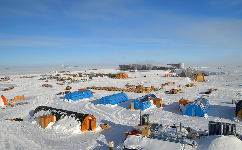 An aerial view of the South Pole Station with numerous support buildings in a snowy landscape.