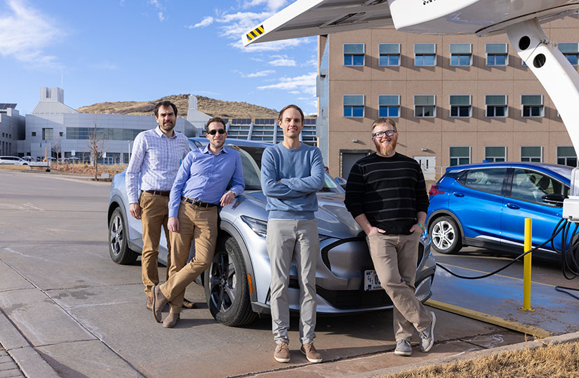 Four men stand in front of an electric vehicle being charged at NREL.