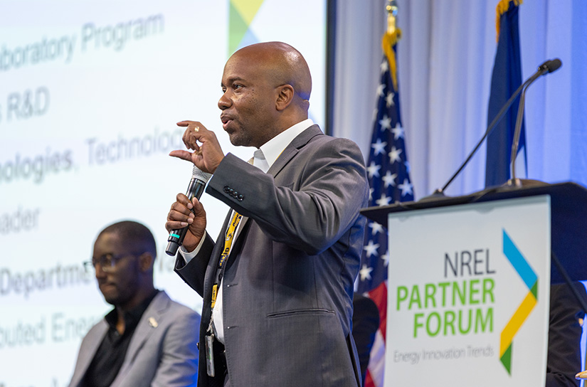 A man in a suit, standing in front of a podium, gestures while addressing a crowd.