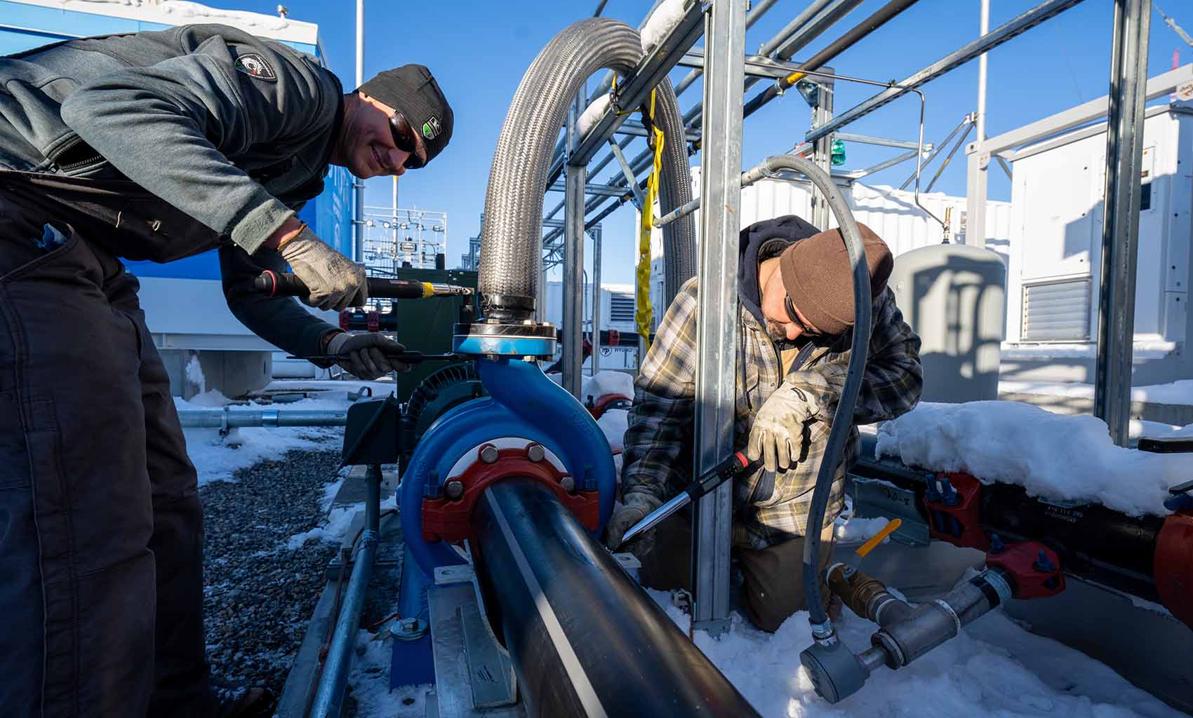 Two people working on equipment outside in the snow.