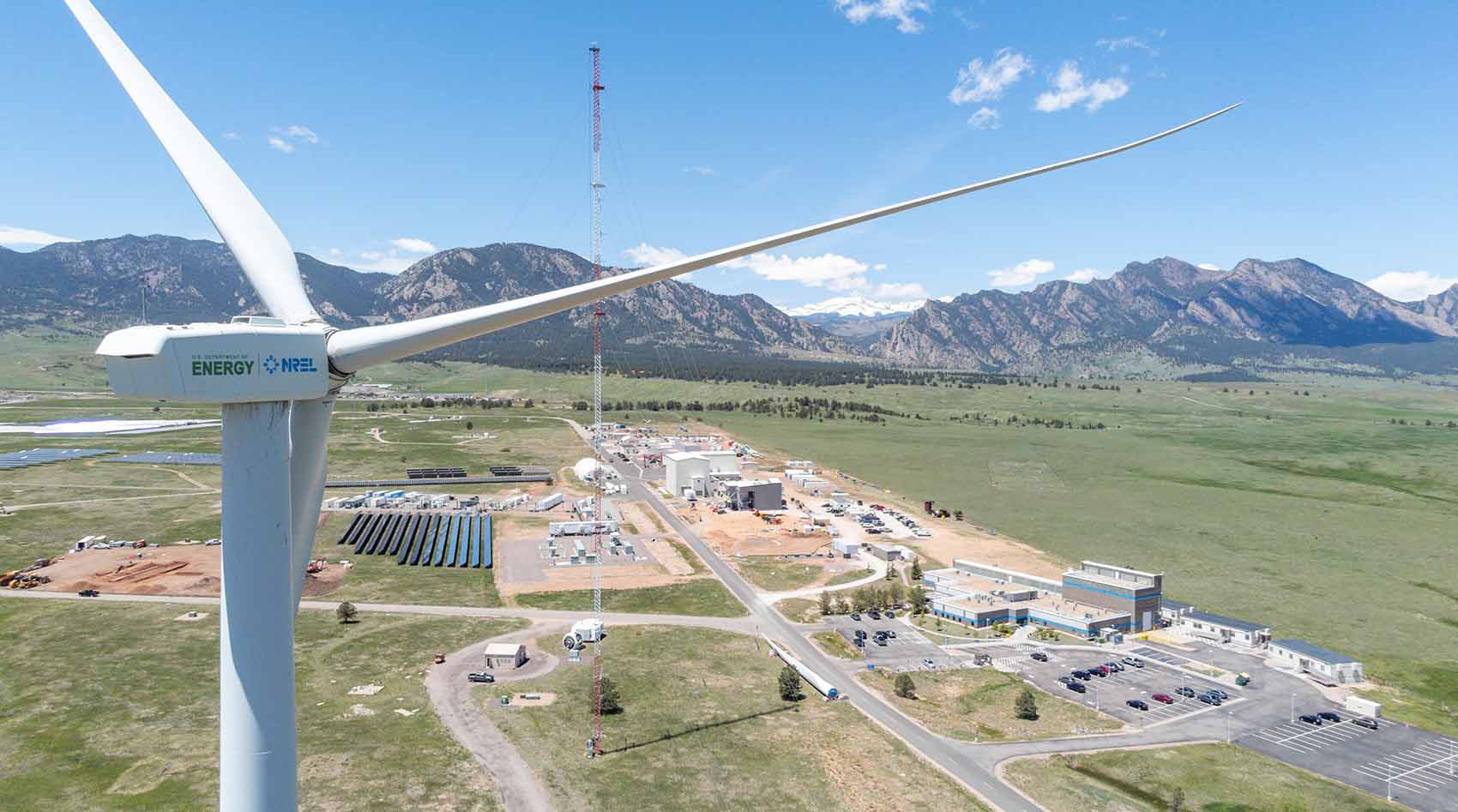 Bird's eye view of a site in front of the rocky mountains with a large wind turbine in the foreground.