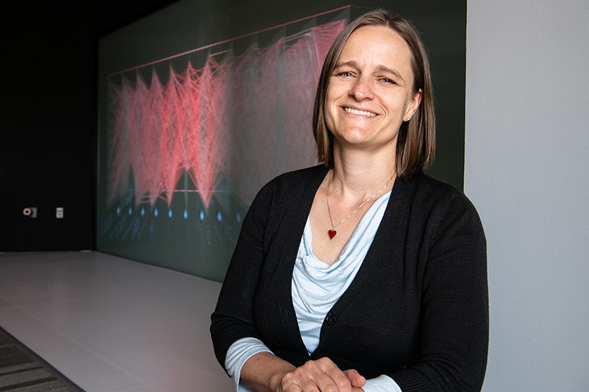 A photo of NREL researcher Emily Newes posing with a large screen displaying data in the background