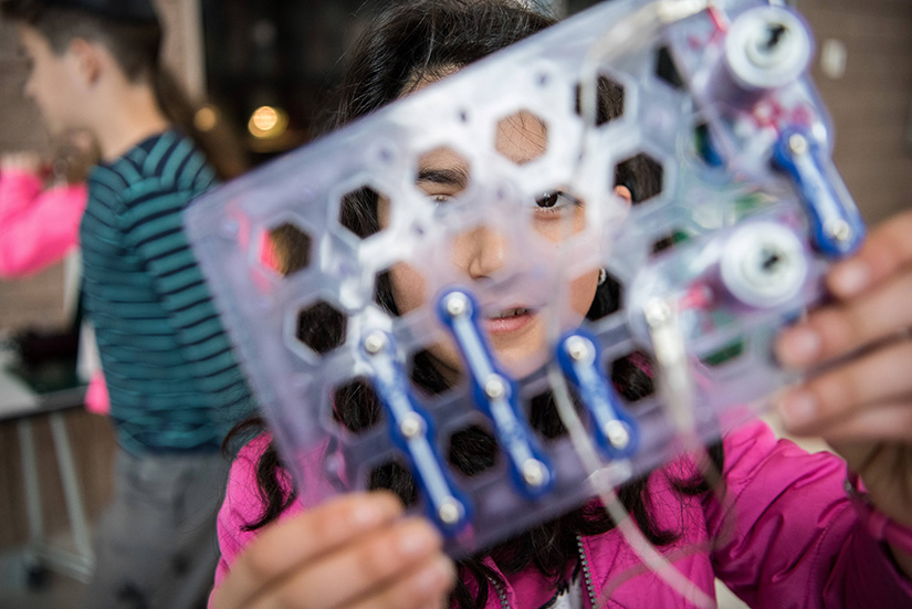 A student holds up in front of her face a scientific device she is working on.