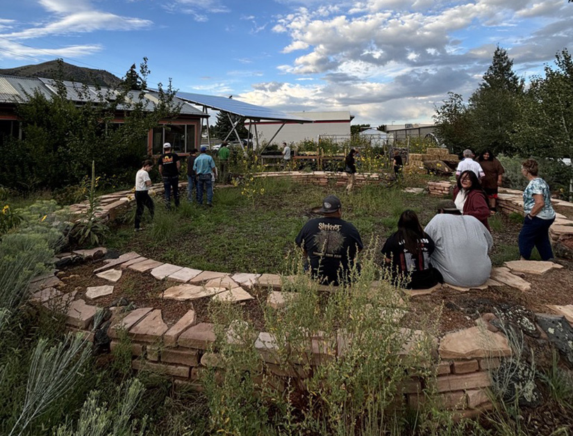 Students sit on a circular rock wall around a garden outside a high school.