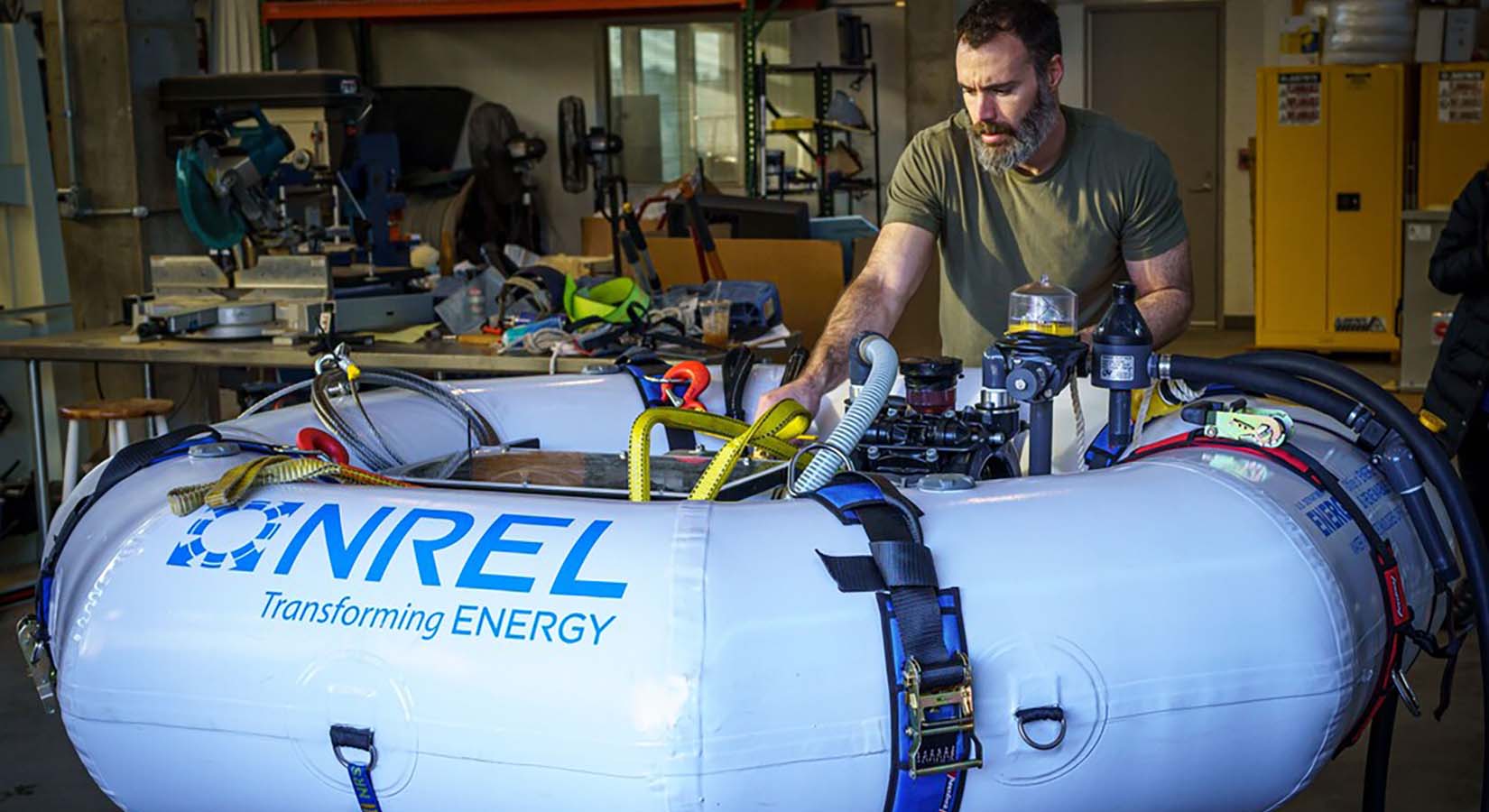 A man stands inside a research lab and examines a machine sitting in an inflatable raft.