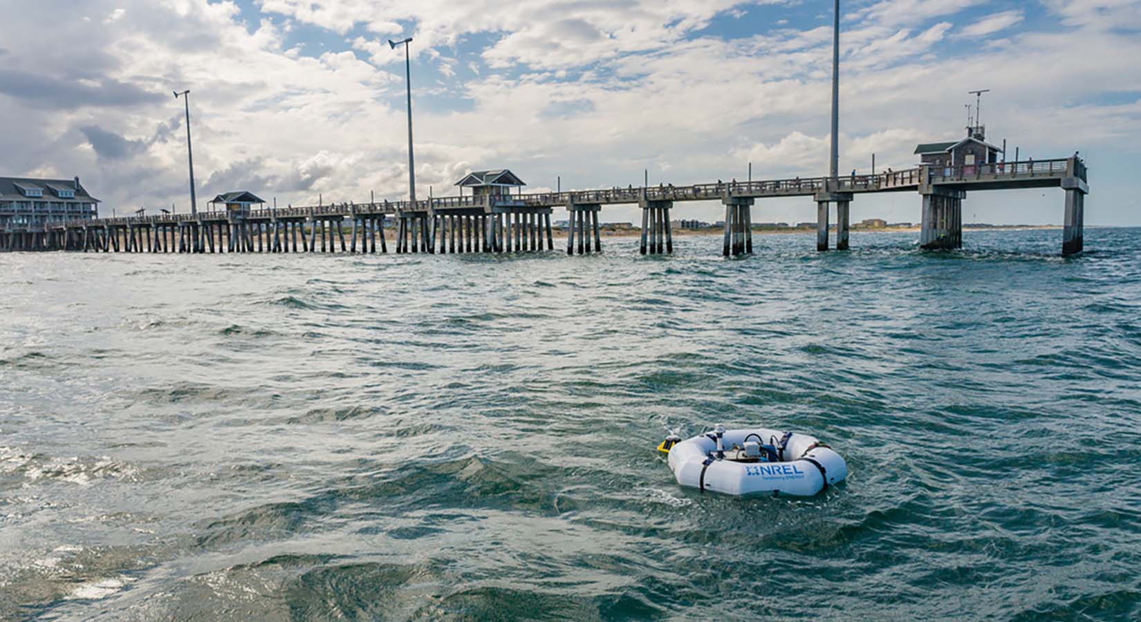 A raft holding a metallic device floats near a long pier.