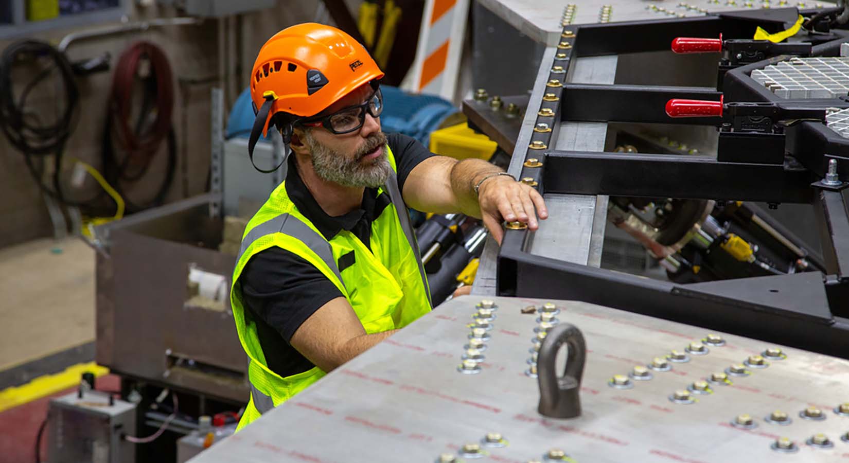  A man in a hardhat and high-vis vest tightens bolts on a metal frame.